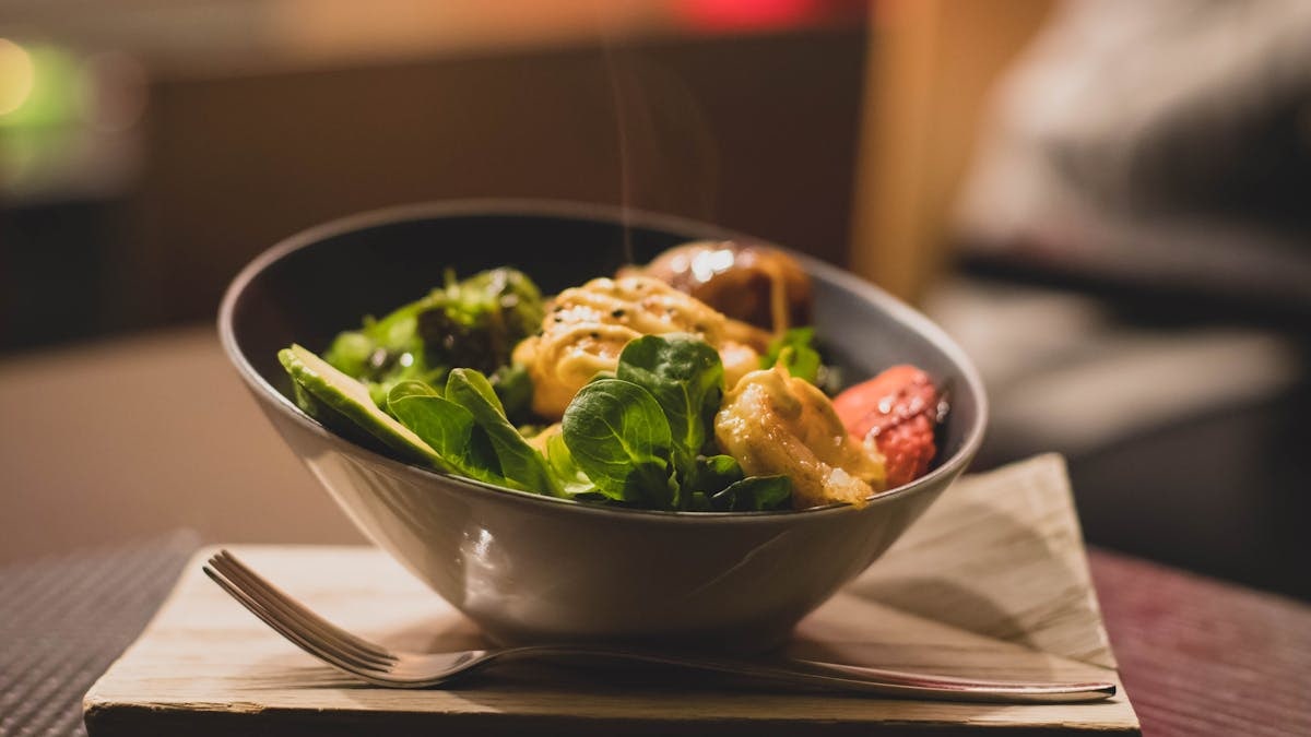 Delicious bowl of salad with fresh greens and grilled chicken served on a wooden platter.